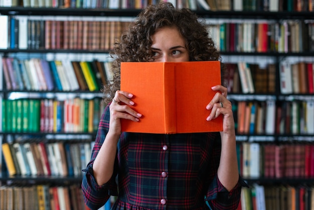 Premium Photo | Playful girl holding a book covering her face and ...