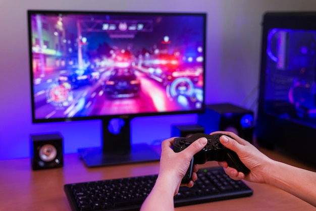 Playing racing games on computer concept. hand holds the joystick. in the background is a gaming computer with rgb light. Premium Photo