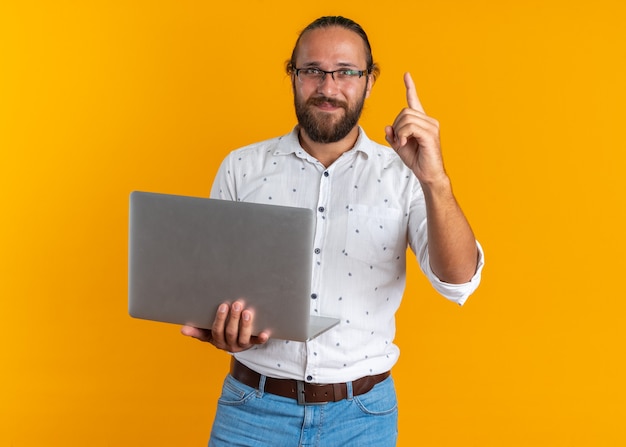 Free Photo Pleased Adult Handsome Man Wearing Glasses Holding Laptop Looking At Camera 4112