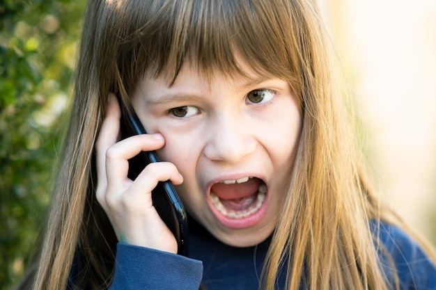 Portrait of angry child girl with long hair talking on cell phone. little female kid having discussion on smartphone. children communication concept. Premium Photo