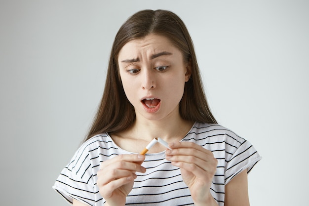 Free Photo Portrait Of Anxious Shocked Young Brunette Female Opening Mouth In Astonishment Having Startled Expression Looking At Last Cigarette That Just Broke In Her Hands Feeling Panic And Desperate