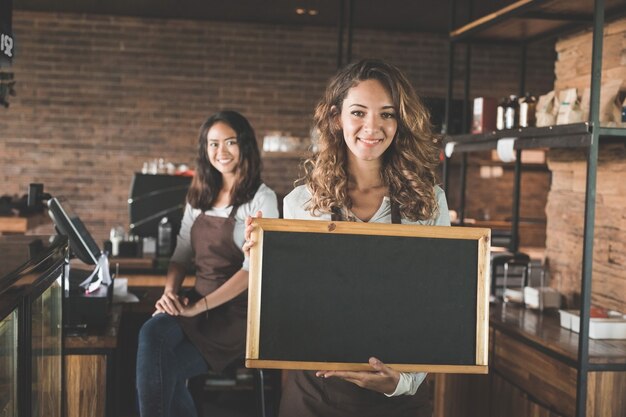 Portrait of attractive female waitress standing and holding blank blackboard sign at a cafe Premium Photo