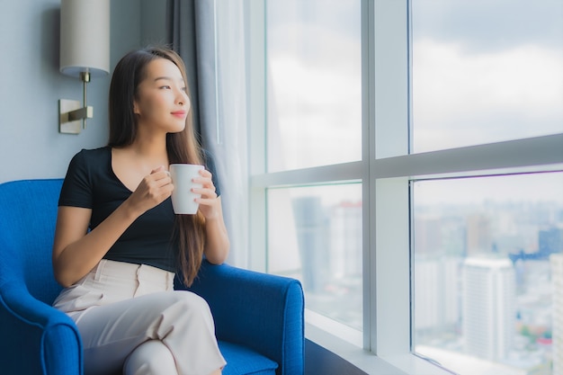 Portrait beautiful young asian woman hold coffee cup on sofa chair in living room area Free Photo