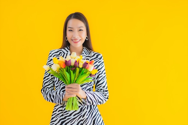 肖像画の美しい若いアジア女性は黄色の花に満足して笑顔します 無料の写真