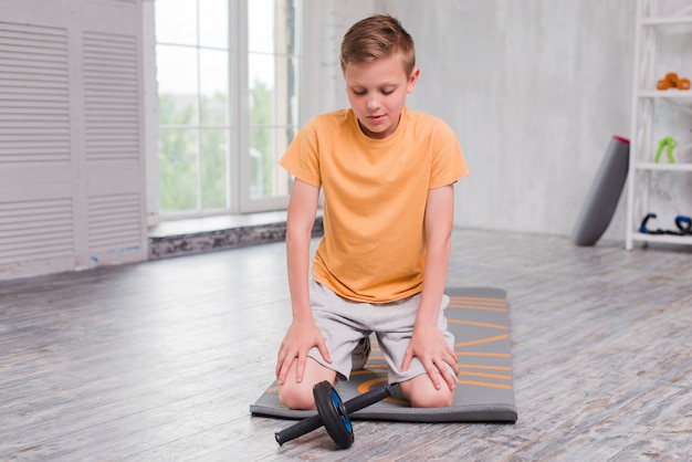 Portrait Of A Boy Kneeling On Exercise Mat Looking At Roller Slide