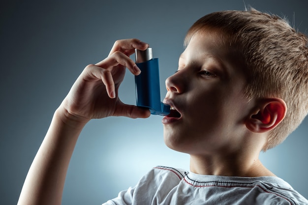 Portrait of a boy using an asthma inhaler to treat inflammatory diseases, shortness of breath. the concept of treatment for cough, allergies, respiratory tract disease. Premium Photo
