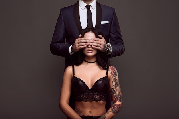 Portrait of a businessman in elegant suit cover eyes of sexy woman with a tattoo in lingerie Free Photo