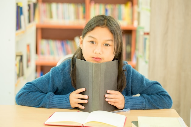 Portrait of clever student with open book reading it in college library Free Photo
