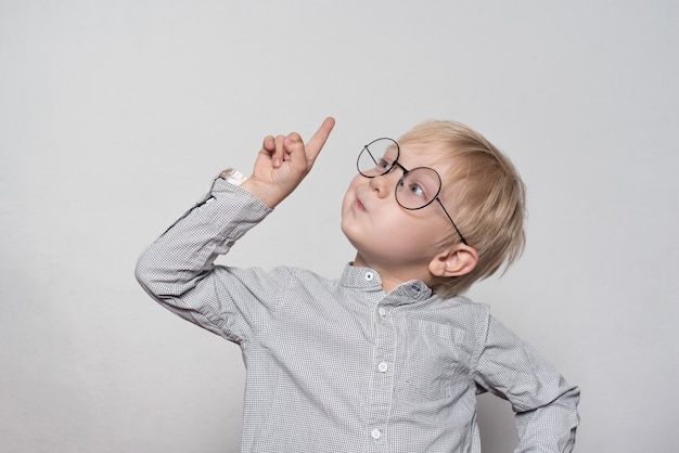Portrait of a cute blond boy with big glasses. finger pointing up. Premium Photo
