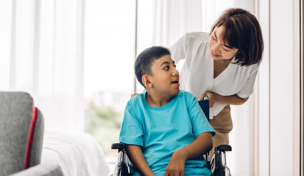 Portrait of enjoy happy love family asian mother playing and carer helping look at disabled son child sitting in wheelchair moments good time at home.disability care concept Premium Photo
