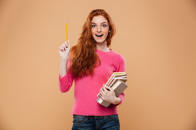 Portrait of an excited pretty redhead girl holding books and having an idea Free Photo