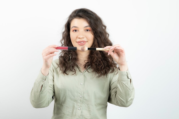 Portrait of fashionable girl model holding brush with lipstick over a white wall . Free Photo