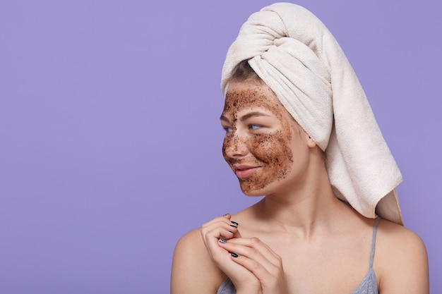 Portrait of female model applies chocolate mask on face, has positive expression, looks aside Free Photo