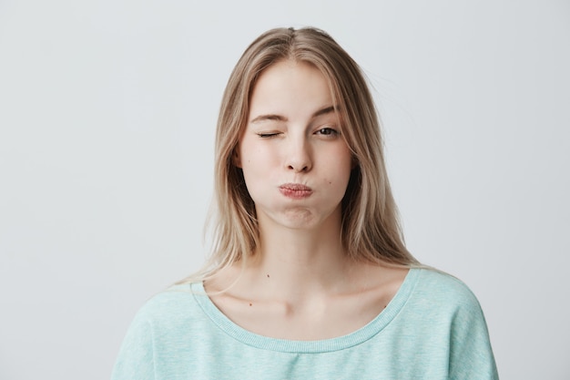 Portrait of frowning blonde young woman pouting her cheeks, blinking ...