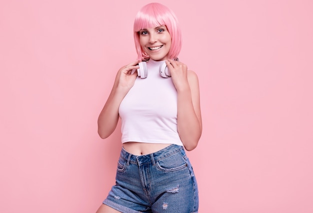 Portrait of gorgeous bright hipster girl with pink hair enjoys the music in headphones on colorful Free Photo