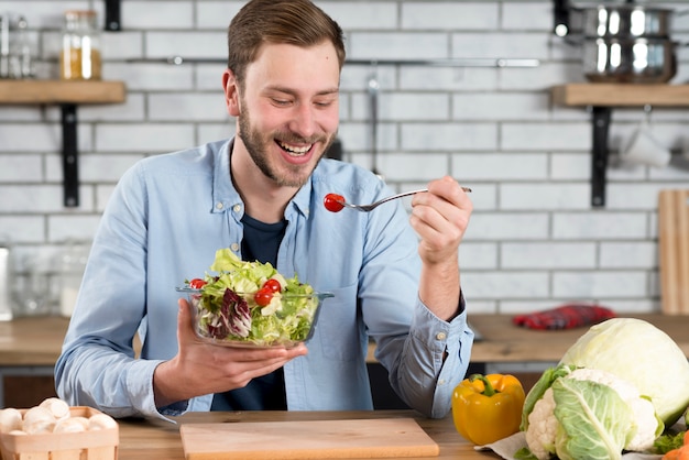 Portrait of a happy man eating fresh salad in the kitchen Free Photo