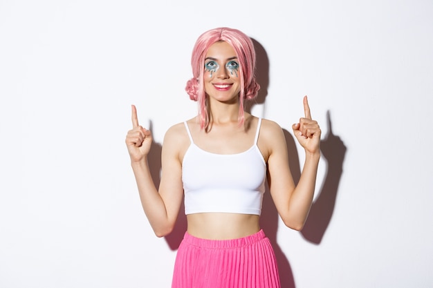 Free Photo Portrait Of Happy Smiling Female Model With Pink Anime Wig And Halloween Makeup Looking Satisfied At Banner Pointing Fingers Up Standing