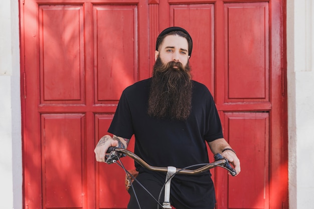Portrait of a long bearded young man siting on bicycle looking at camera Free Photo