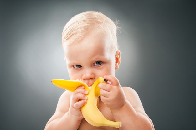 Premium Photo | Portrait Of Lovely Baby Eating Banana Over Grey Background