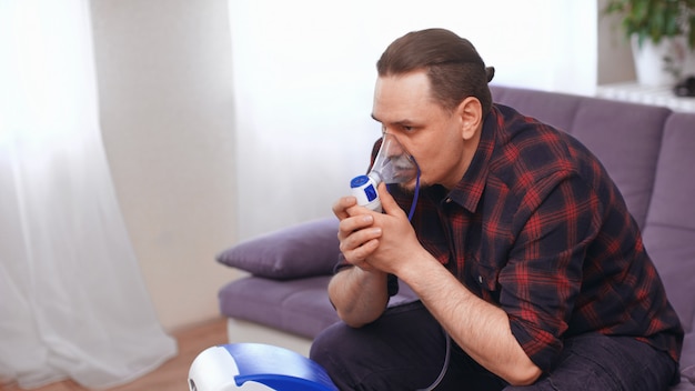 Portrait of a man breathing through an inhaler mask at home. Premium Photo