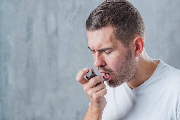 Portrait of a man with closed eyed using asthma inhaler Free Photo