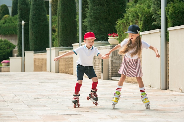 公園でローラースケートで一緒にスケートをする魅力的な10代のカップルの肖像画 10代の白人の男の子と女の子 子供たちのカラフルな服 ライフスタイル 流行色の概念 無料の写真