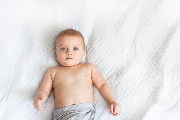 9ヶ月のかわいい赤ちゃんの肖像画 小さな男の子はベッドで何が起こっているのか興味を持って見ています プレミアム写真