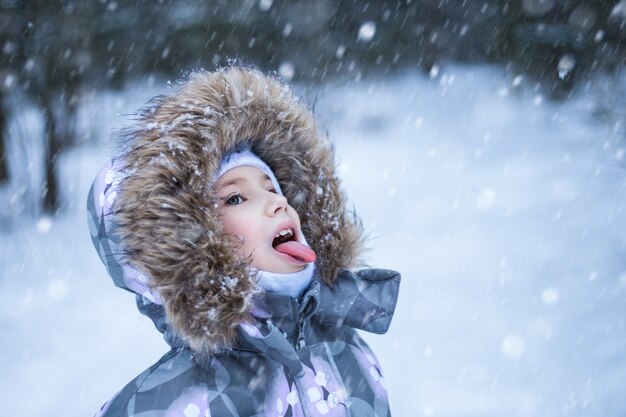 冬の日に口で雪をキャッチするかわいい女の子の肖像画 プレミアム写真