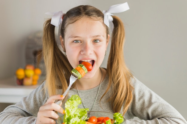 フォークと新鮮な野菜サラダを食べる女の子の肖像 無料の写真