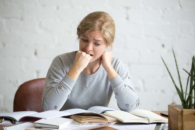 Portrait of a student girl sitting at the desk biting her fist Free Photo