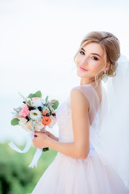 Portrait of a stunning bride with blonde hair holding peach wedding bouquet in her arms Free Photo