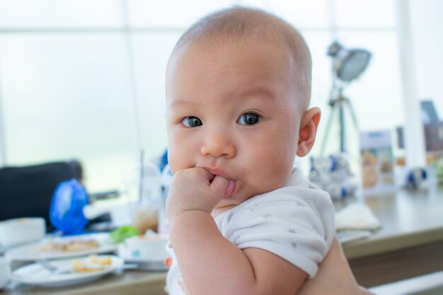 彼女の拳を口に入れて自分の指をかむ愛らしい笑顔の赤ちゃんの肖像画 プレミアム写真