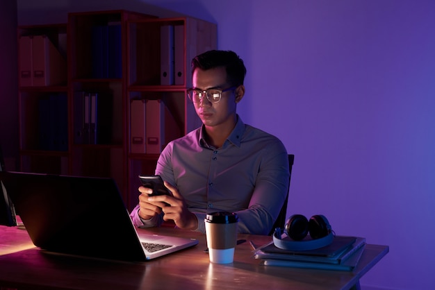ノートパソコンに座って暗い部屋でアジア人男性のテキストメッセージの肖像画 無料の写真