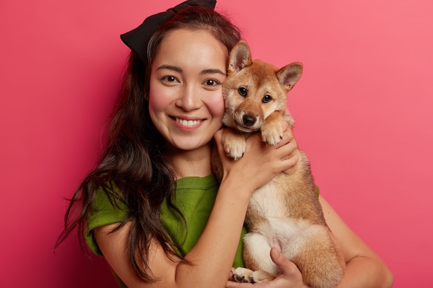 思いやりのある混血の女性の肖像画は 血統の子犬を顔に近づけ 柴犬を抱きしめ 楽しい時間を過ごし 家庭的なリラックスを楽しみ 永遠に一緒にいて スタジオでリラックスします 無料の写真