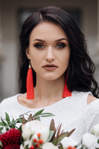 Portrait of charming brunette bride in white dress with red accessories Free Photo