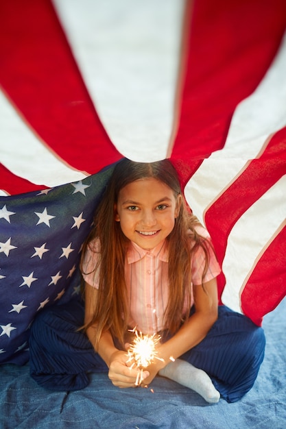 アメリカの国旗に覆われた笑顔の輝く光を保持しているかわいい女の子の肖像画 プレミアム写真