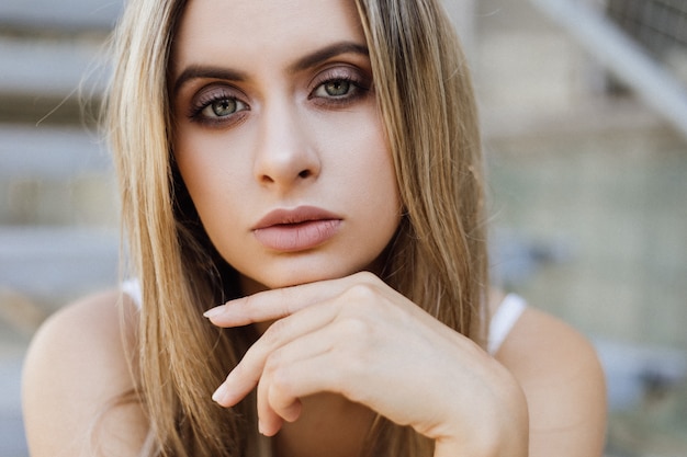 Portrait of gorgeous blonde woman sitting on the concrete footsteps Free Photo