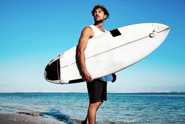 青い海と空にサーフボードで行くカジュアルな服を着てハンサムなヒップスター日光浴ファッション男モデルサーファーの肖像 無料の写真