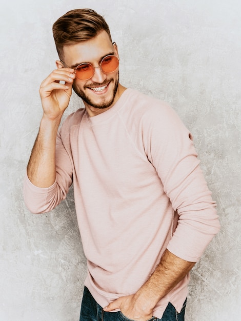 カジュアルな夏のピンクの服を着てハンサムな笑みを浮かべて若い男モデルの肖像画 丸いサングラスでポーズをとってファッションスタイリッシュな男 無料の写真