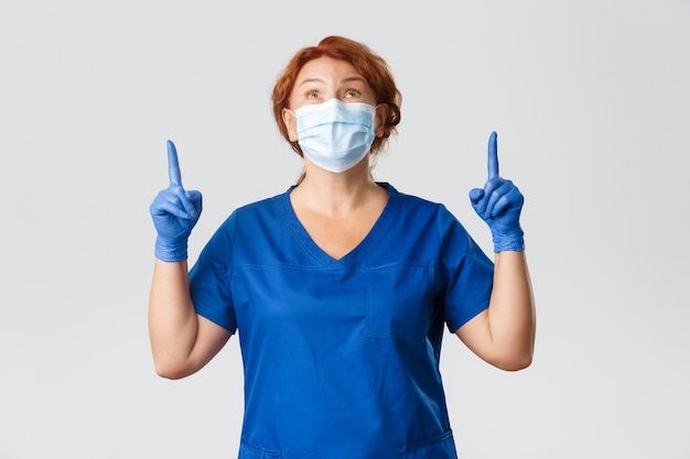 幸せな医者の肖像画は上向きに何かを賞賛し フェイスマスクと手袋をはめた女性看護師は賞賛を見て上向きにしています 無料の写真