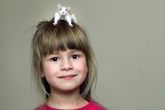 光の壁の頭の上の白いペットのマウスハムスターと幸せな笑顔面白いかわいい子少女の肖像画 自宅でペットを飼い ケアと動物愛のコンセプト プレミアム写真