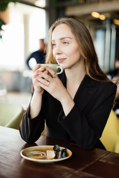 レストランで朝のコーヒーを飲みながら手でマグカップを持つ幸せな若い女性の肖像画 無料の写真