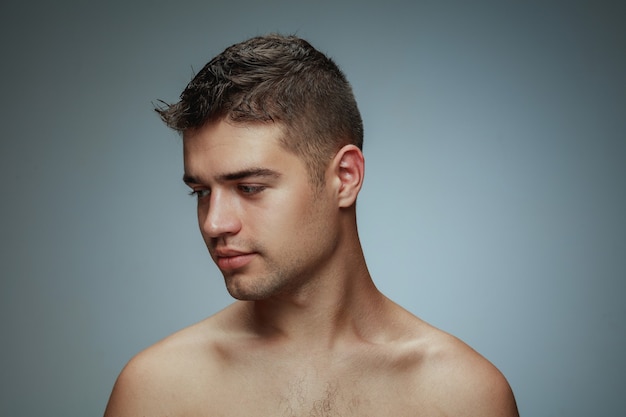灰色の背景に分離された上半身裸の若い男の肖像画 側面を見てポーズをとる白人の健康な男性モデル 無料の写真