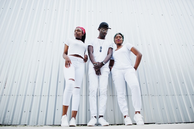 2人の女の子とスタイリッシュなアフリカ系アメリカ人の男の肖像は 鋼の壁に対して 白い服を着ます 若い黒人のストリートファッション プレミアム写真