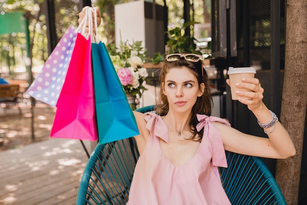 コーヒー 夏のファッションの服 ピンクのコットンドレス トレンディなアパレルを飲んで買い物袋とカフェに座っている若い魅力的な女性の肖像画は困惑して考えて 無料の写真