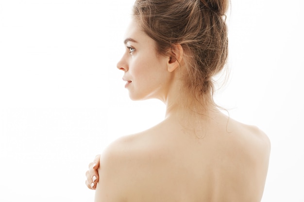 白い背景の上に立っている若い美しい柔らかい裸の女性の肖像画。 無料の写真
