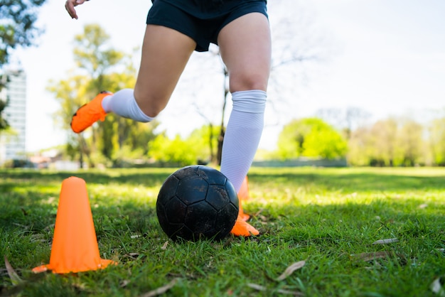フィールド上でボールを練習しながらコーンの周りを実行している若い女性のサッカー選手の肖像画 スポーツコンセプト 無料の写真