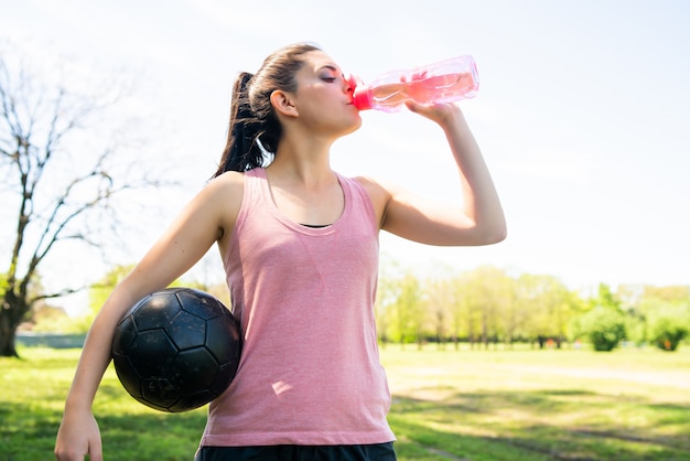 ピッチで休憩し ボトルから水を飲む若い女性サッカー選手の肖像画 無料の写真