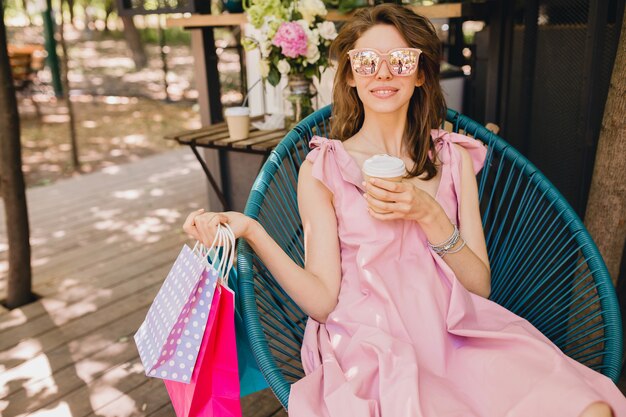 コーヒー 夏のファッションの服 ピンクのコットンドレス トレンディなアパレルを飲むショッピングバッグのカフェに座っている若い笑顔幸せな魅力的な女性の肖像画 無料の写真