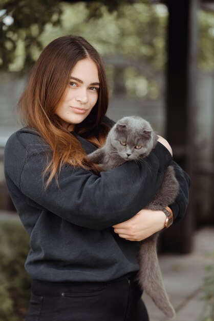 茶色の目でかわいいブリティッシュショートヘアの猫を保持している若い女性の肖像画 愛らしい国内ペットのコンセプト プレミアム写真